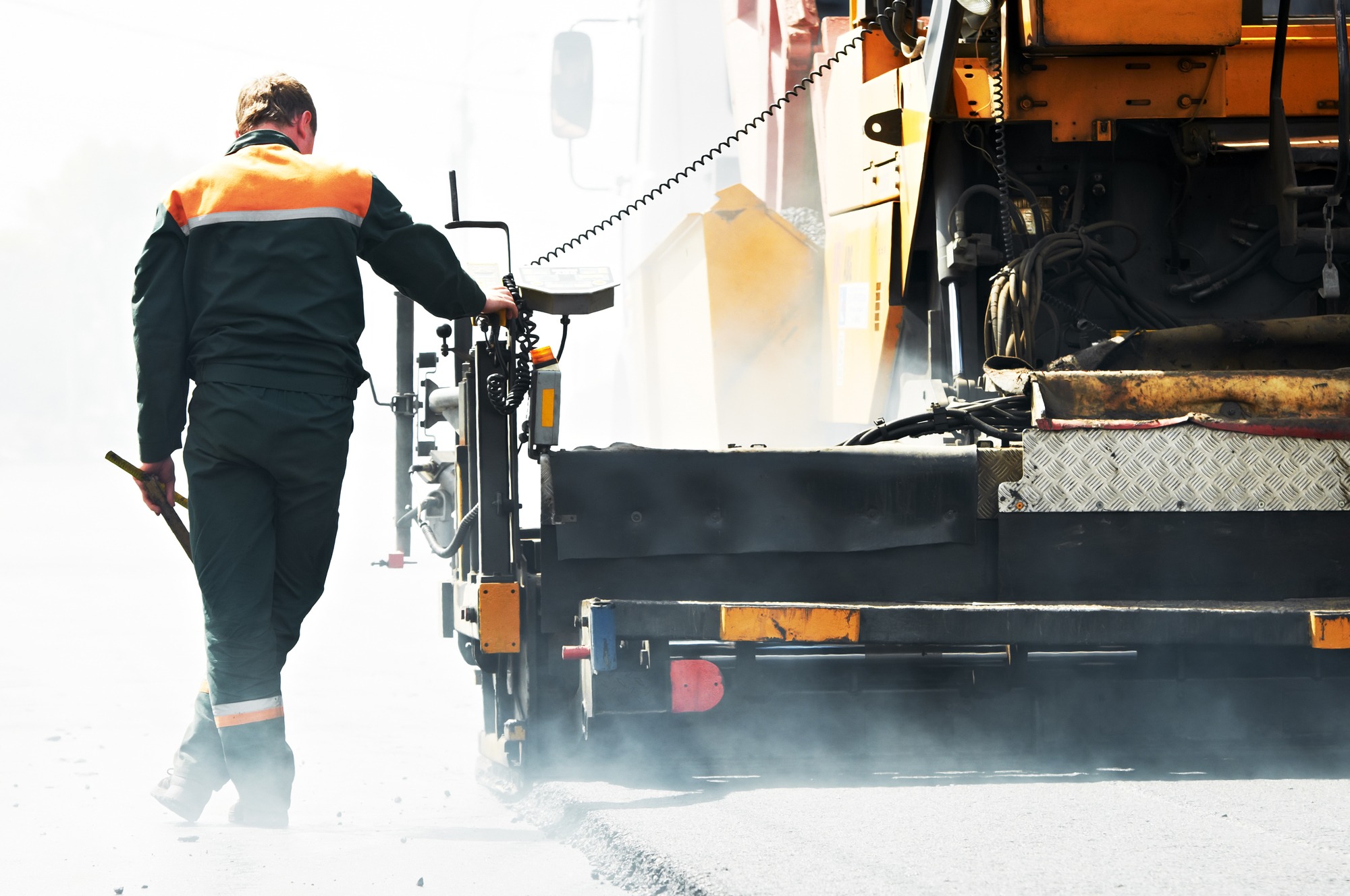 Worker operating asphalt paver machine during road construction and repairing works