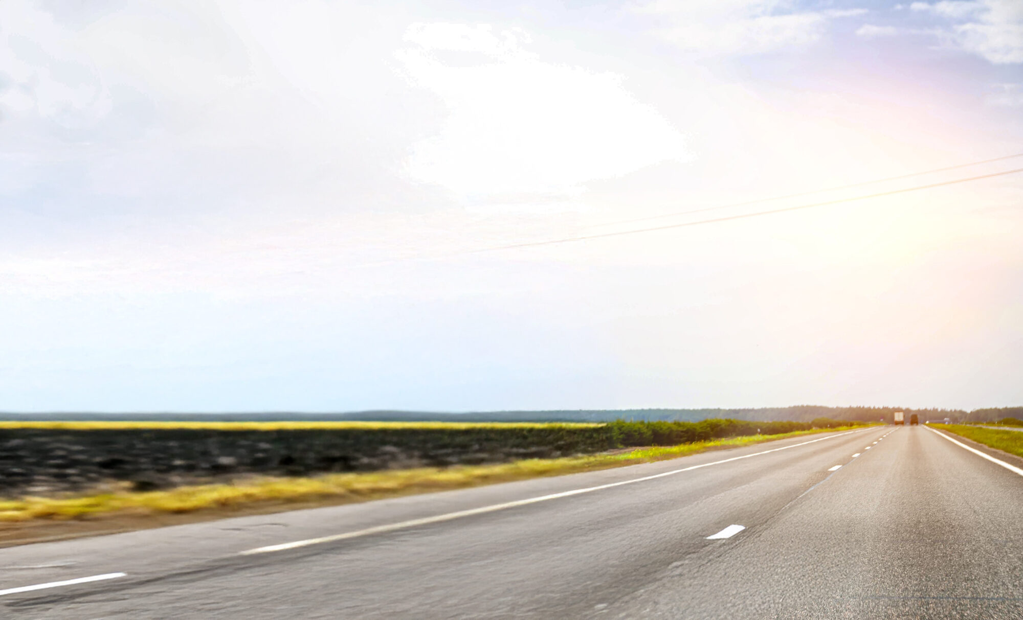 A clear, empty highway stretches ahead, illuminated by a bright sun shining in the background.