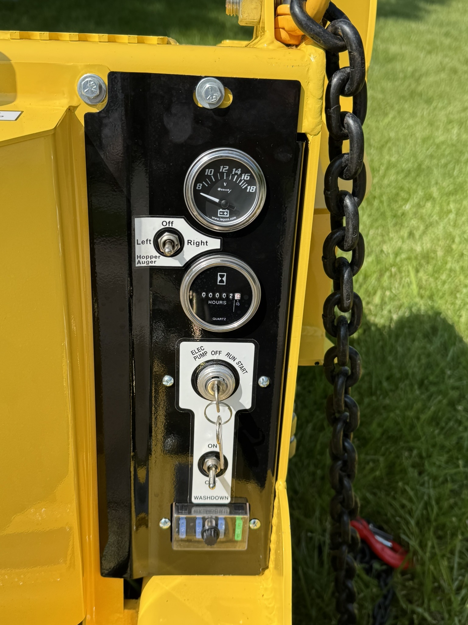 Control panel of a yellow piece of machinery featuring gauges, switches for auger direction, an hour meter, and a washdown function.